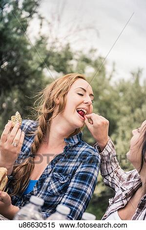 Stock Photography - Young woman feeding best friend cherries at picnic table. Fotosearch