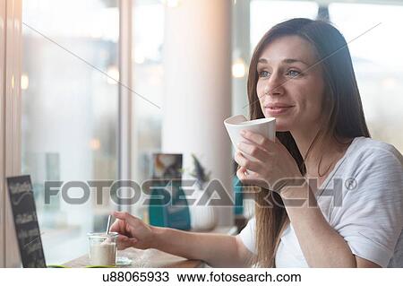 Stock Image - Young woman gazing out through cafe window. Fotosearch