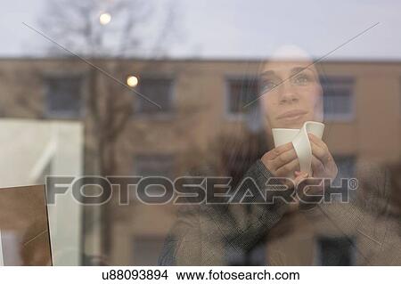 Picture - Young woman gazing through cafe window. Fotosearch
