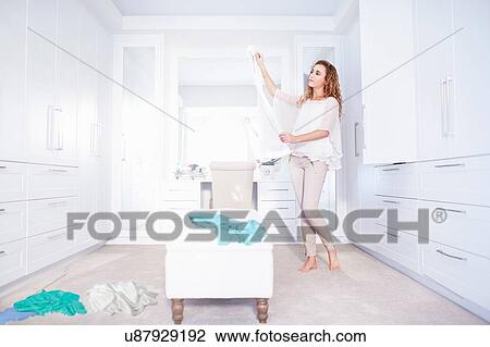 Stock Image - Young woman getting ready and deciding on clothes in bedroom. Fotosearch