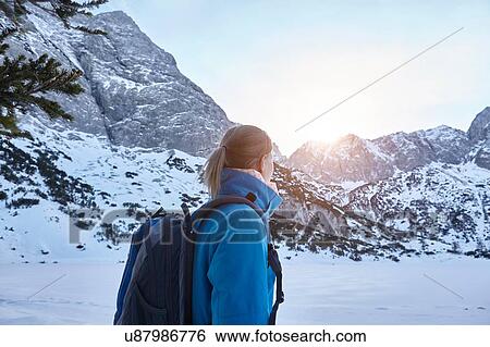 Stock Photograph - Young woman hiking in snow and watching the sun on mountain top, Austria. Fotosearch