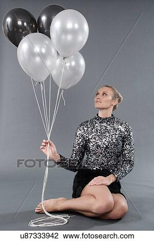 Stock Image - Young woman holding black and white balloons, grey background. Fotosearch