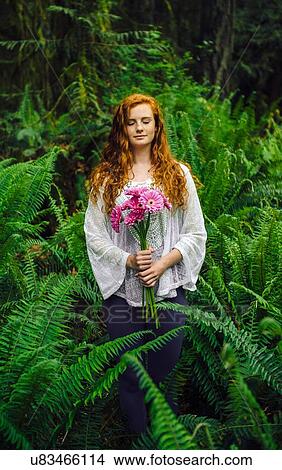 Picture - Young woman holding bunch of pink gerberas amongst forest ferns. Fotosearch