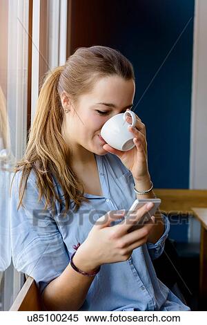 Young woman holding smartphone drinking coffee View Large Photo Image Stock Photography - Young woman holding smartphone drinking coffee. Fotosearch