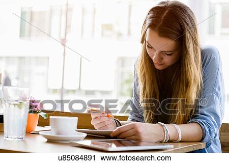 Young woman in cafe looking down writing View Large Photo Image Stock Image - Young woman in cafe looking down writing. Fotosearch