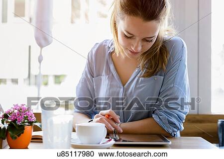 Stock Image - Young woman in cafe writing, looking at camera smiling. Fotosearch