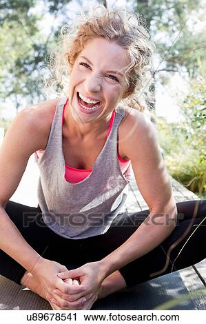 Stock Image - Young woman in sports clothes sitting on floor, laughing. Fotosearch