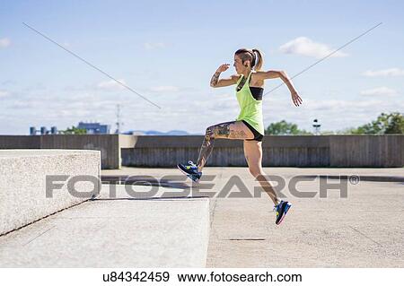 Stock Photo - Young woman jumping up large concrete step. Fotosearch