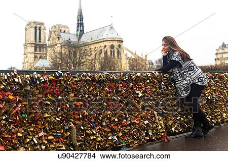 Picture - Young woman leaning against love locks, Pont de l'archeveche, Notre Dame Cathedral in background, Paris, France. Fotosearch