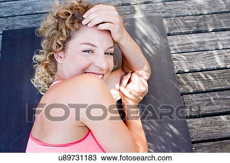 Young woman lying down on yoga mat, portrait View Large Photo Image Stock Image - Young woman lying down on yoga mat, portrait. Fotosearch