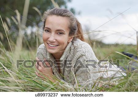Young woman lying on front on grass looking at camera smiling View Large Photo Image Stock Photo - Young woman lying on front on grass looking at camera smiling. Fotosearch