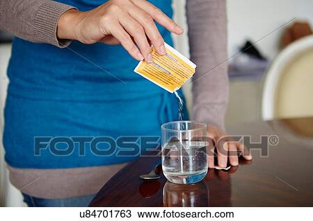 Stock Image - "Young woman mixing water-soluble medication from sachet, in glass of water". Fotosearch