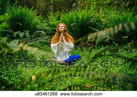 Stock Photo - Young woman practicing yoga in lotus position in forest. Fotosearch