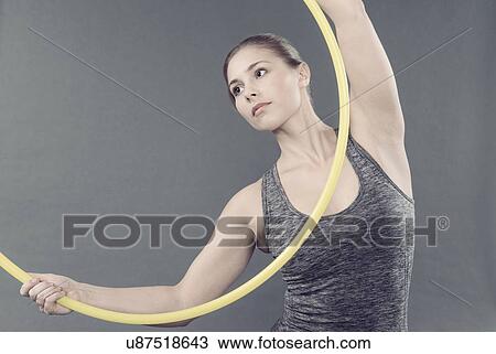 Stock Image - Young woman practising with hula hoop, grey background. Fotosearch