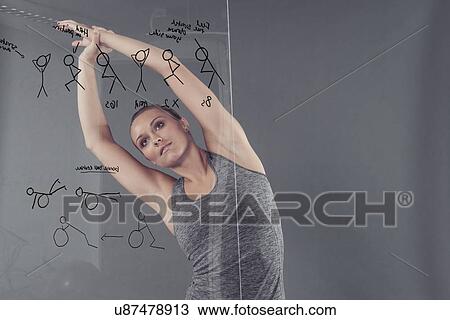 Stock Image - Young woman practising yoga in front of glass wall, grey background. Fotosearch