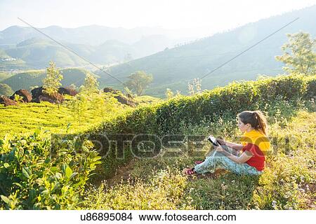 Picture - Young woman reading digital tablet at tea plantations near Munnar, Kerala, India. Fotosearch