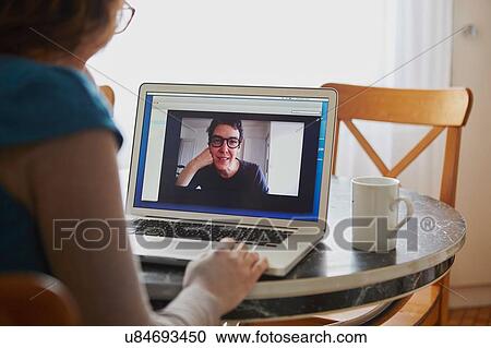 "Young woman sitting at table, using laptop, on video call with mature woman, rear view" View Large Photo Image Stock Image - "Young woman sitting at table, using laptop, on video call with mature woman, rear view". Fotosearch