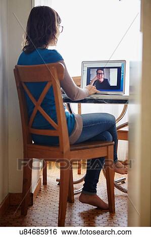 "Young woman sitting at table, using laptop, on video call with mature woman, rear view" View Large Photo Image Stock Photograph - "Young woman sitting at table, using laptop, on video call with mature woman, rear view". Fotosearch