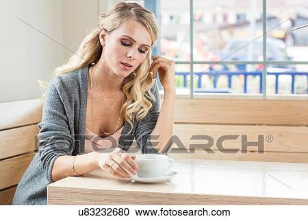 Young woman sitting at table with cup and saucer looking down View Large Photo Image Stock Image - Young woman sitting at table with cup and saucer looking down. Fotosearch