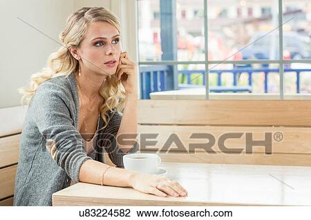 Stock Image - Young woman sitting at table with teacup looking away. Fotosearch