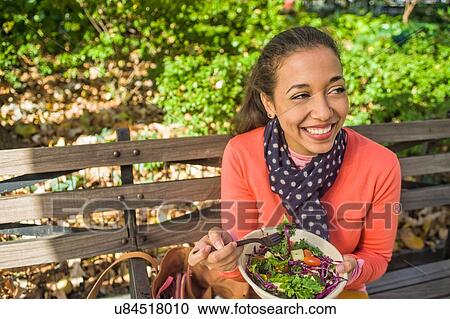 Young woman sitting on park bench eating lunch View Large Photo Image Stock Image - Young woman sitting on park bench eating lunch. Fotosearch