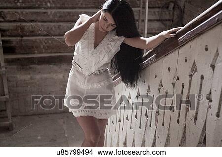 Picture - Young woman standing against railing of staircase. Fotosearch