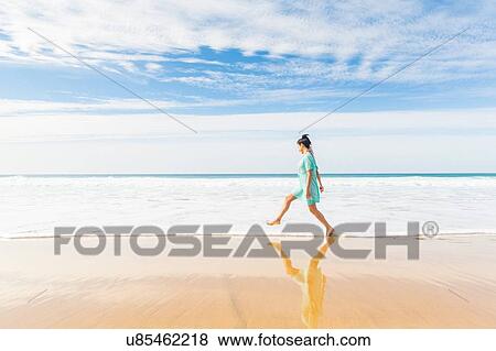 Stock Photo - Young woman stepping into ocean waves on beach, El Cotillo, Fuerteventura, Spain. Fotosearch