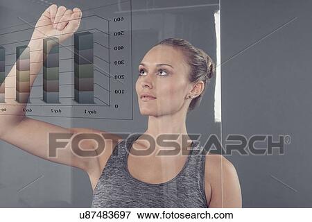 Stock Photo - Young woman studying chart on glass wall, grey background. Fotosearch
