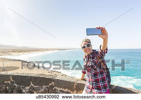 Young woman taking smartphone selfie at coast, El Cotillo, Fuerteventura, Spain View Large Photo Image Stock Image - Young woman taking smartphone selfie at coast, El Cotillo, Fuerteventura, Spain. Fotosearch