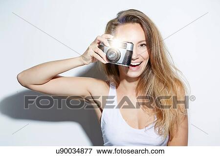 Stock Photo - Young woman using camera looking at camera smiling. Fotosearch