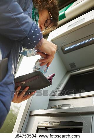 "Young woman using cash machine, putting money in purse, low angle view" View Large Photo Image Picture - "Young woman using cash machine, putting money in purse, low angle view". Fotosearch