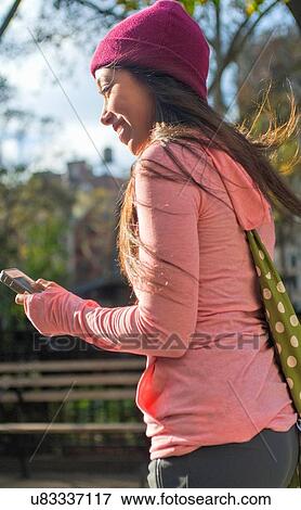 Stock Photo - Young woman using smartphone in park. Fotosearch