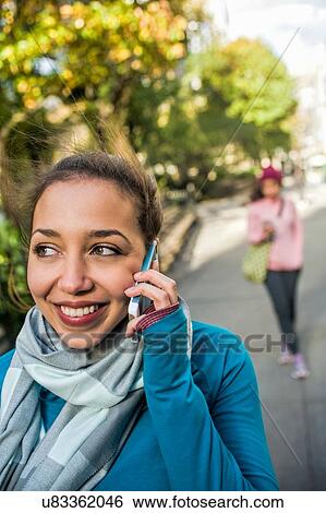 Stock Photograph - Young woman using smartphone in park. Fotosearch