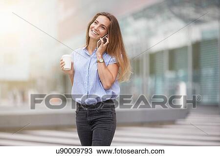 Stock Image - Young woman using smartphone to make telephone call looking away smiling. Fotosearch