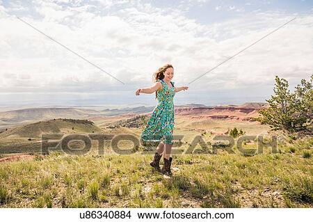 Picture - Young woman wearing dress and cowboy boots dancing in hilly landscape, Bridger, Montana, USA. Fotosearch