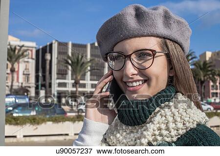 Stock Photo - Young woman wearing eyeglasses using smartphone looking away smiling. Fotosearch