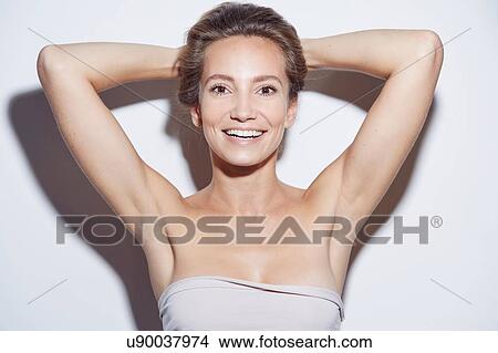 Picture - Young woman wearing tube top, hands behind head looking at camera smiling. Fotosearch