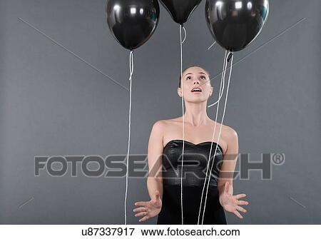 Stock Photo - Young woman with black balloons, grey background. Fotosearch