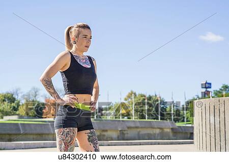 "Young woman with tattoos, exercising, standing with hands on hips, outdoors" View Large Photo Image Stock Image - "Young woman with tattoos, exercising, standing with hands on hips, outdoors". Fotosearch