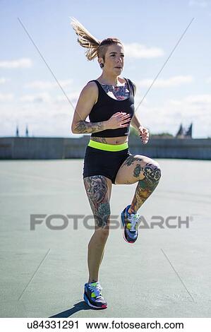 Stock Image - "Young woman with tattoos, exercising, running on spot". Fotosearch