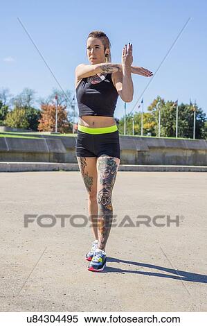 Stock Photography - "Young woman with tattoos, exercising, stretching arms". Fotosearch