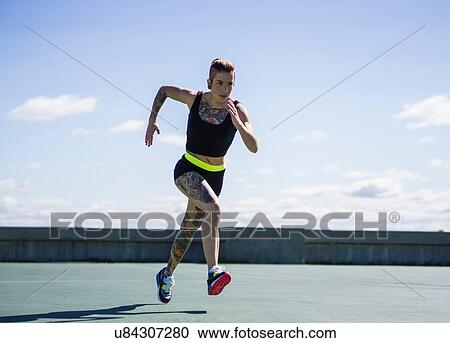 Stock Image - "Young woman with tattoos, running, outdoors". Fotosearch