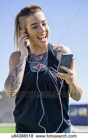 "Young woman with tattoos, using smartphone, wearing earphones, outdoors" View Large Photo Image Stock Photo - "Young woman with tattoos, using smartphone, wearing earphones, outdoors". Fotosearch
