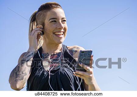 "Young woman with tattoos, using smartphone, wearing earphones, outdoors" View Large Photo Image Stock Photography - "Young woman with tattoos, using smartphone, wearing earphones, outdoors". Fotosearch