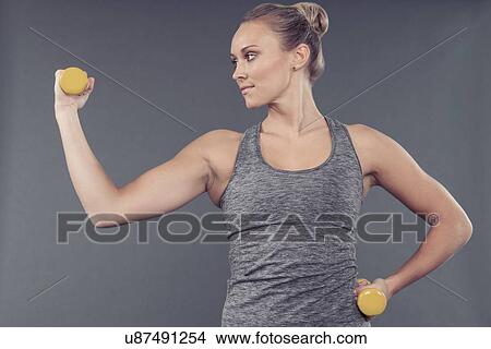Young woman working out with dumbbells, grey background View Large Photo Image Picture - Young woman working out with dumbbells, grey background. Fotosearch