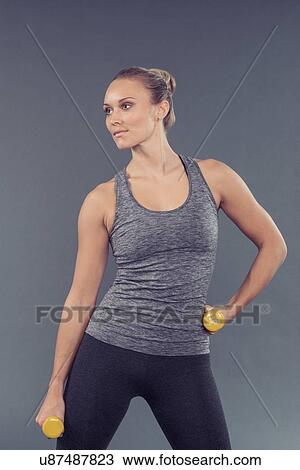 Young woman working out with dumbbells, grey background View Large Photo Image Stock Image - Young woman working out with dumbbells, grey background. Fotosearch