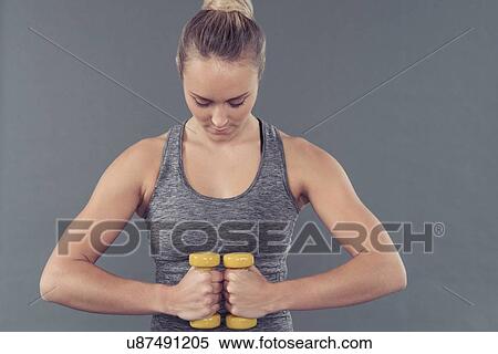 Stock Photography - Young woman working out with dumbbells, grey background. Fotosearch