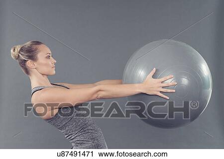 Stock Image - Young woman working out with gym ball, grey background. Fotosearch