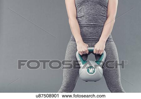 Stock Image - Young woman working out with kettlebell, grey background. Fotosearch