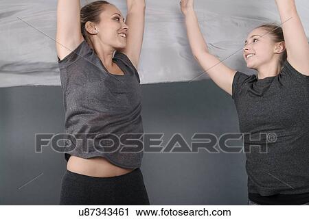 Stock Image - Young women holding cloth over head, grey background. Fotosearch